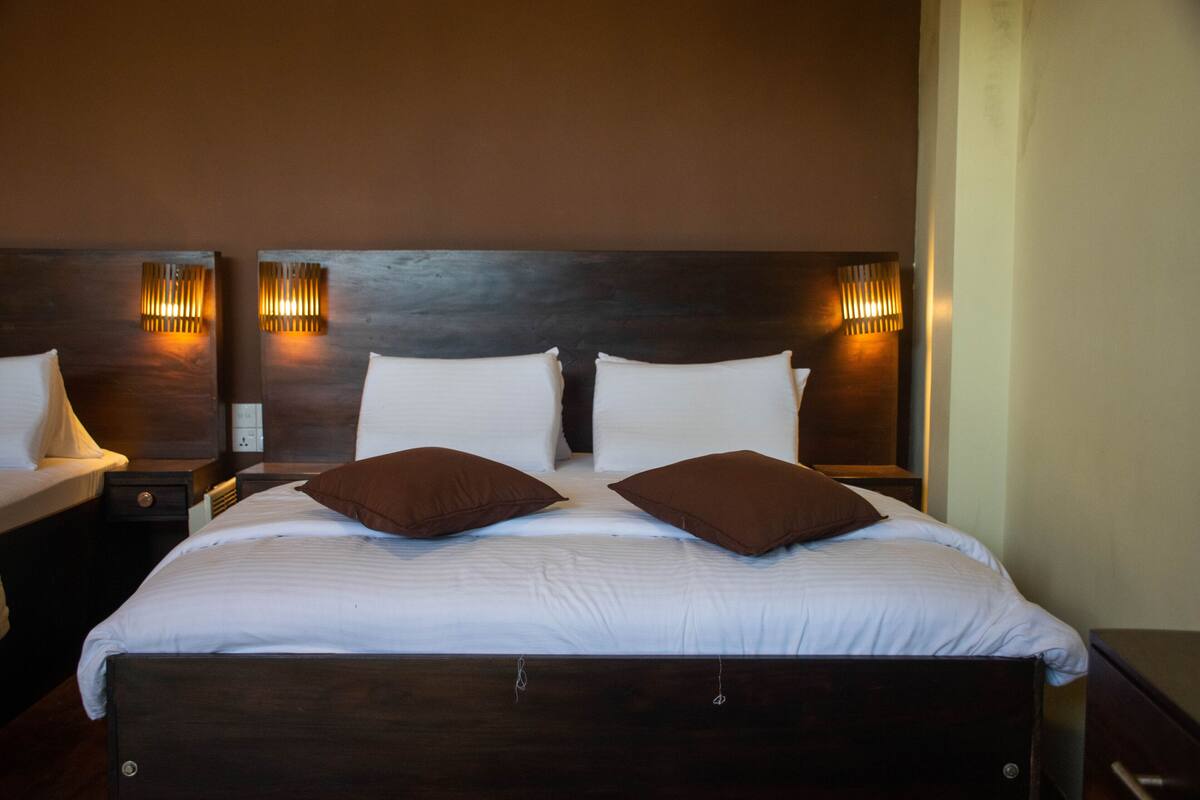 Una cama bien hecha con dos almohadas, un cabecero de madera y dos lámparas de pared.