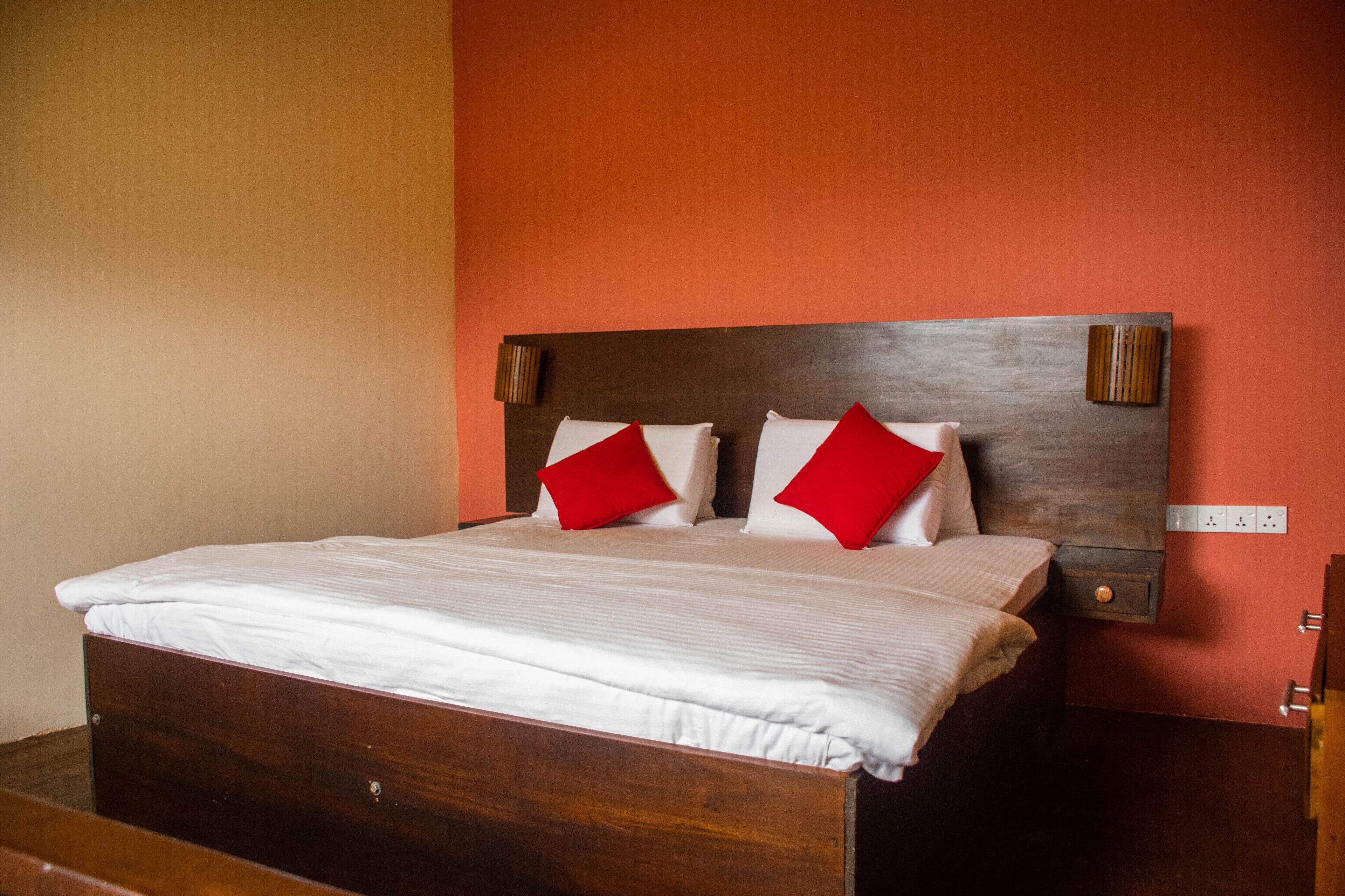 A bed with a wooden frame and white bedding, two red pillows, and a wooden headboard with wall-mounted lamps.
