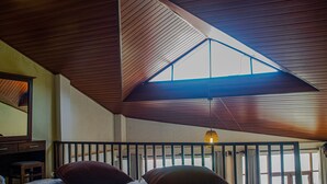 Une chambre avec un plafond en pente, un lit avec deux oreillers, un bureau en bois et un luminaire suspendu.