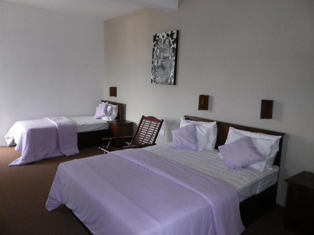 Habitación de hotel con dos camas individuales, una cama grande y una silla.