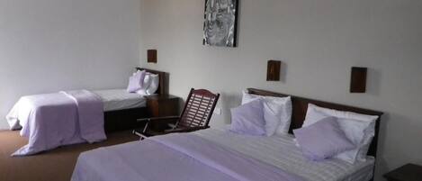 A hotel room with two single beds, a large bed, and a chair.