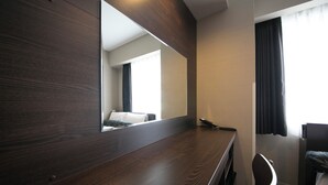 A hotel room with a wooden desk, a large mirror, a bed, and a window with curtains. - Just Inn Premium Nagoya Station (Nagoya)
