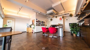 Un interior moderno con mostrador de recepción, sillas rojas, una zona de cocina y una estantería.