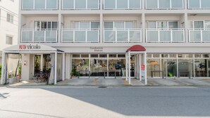 Un edificio de varios pisos con entrada a nivel de calle, un área de espera techada y un escaparate visible.