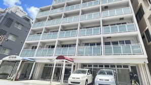 Un edificio de varios pisos con fachada blanca, balcones y un área de entrada cubierta.