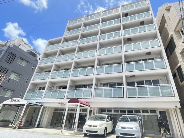Un edificio de varios pisos con fachada blanca, balcones y un área de entrada cubierta.