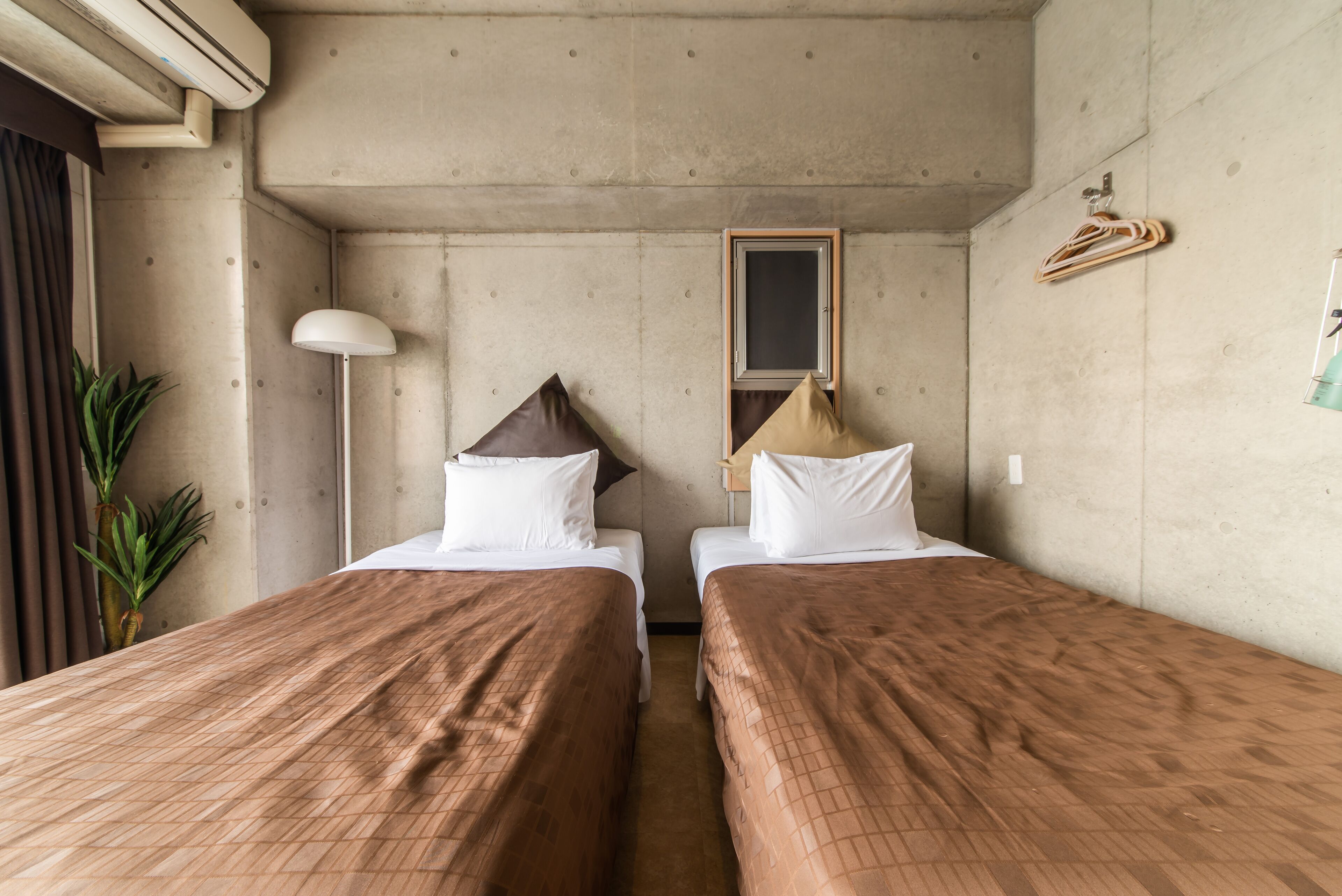 A room with two beds, a hanging light, a mirror, and a plant.
