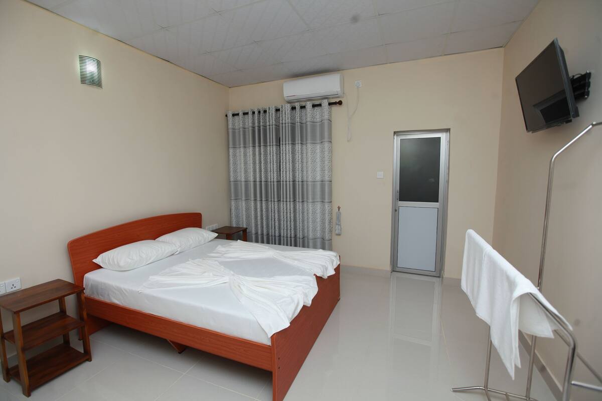 A bedroom with a wooden bed, a bedside table, a curtain, a TV mounted on the wall, and a door.