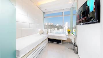 Quarto moderno com um banco embutido, uma janela grande com vista para a cidade e uma televisão de tela plana fixada na parede.