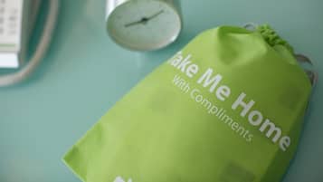 A green bag with the text "Take Me Home With Compliments" on a teal surface.