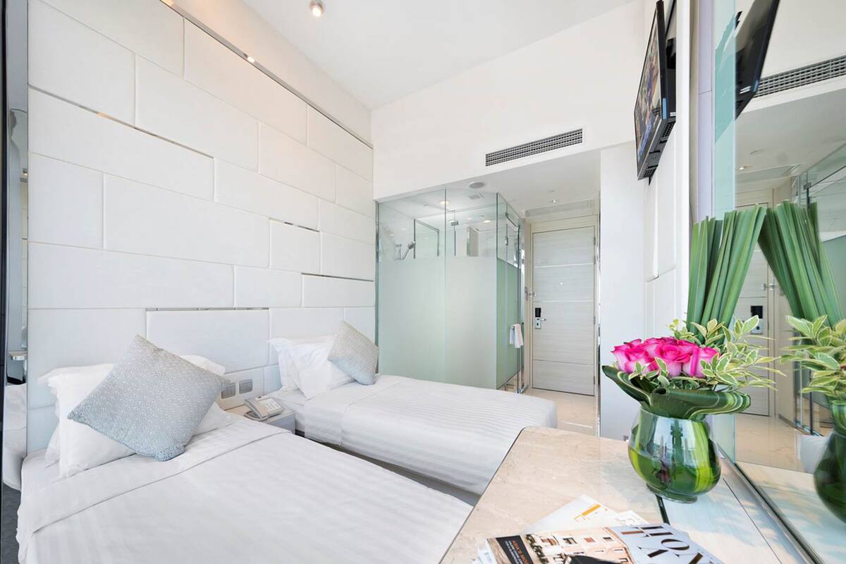 A hotel room with two beds, a mirror, a vase with flowers, and a view of the bathroom.