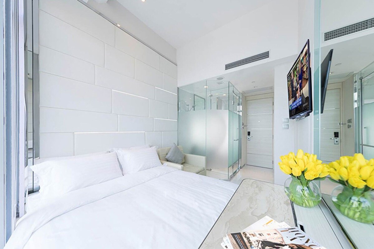 Ein modernes Hotelzimmer mit einem großen Bett, einer Glasdusche, einem Flachbildfernseher und einer Vase mit gelben Blumen.