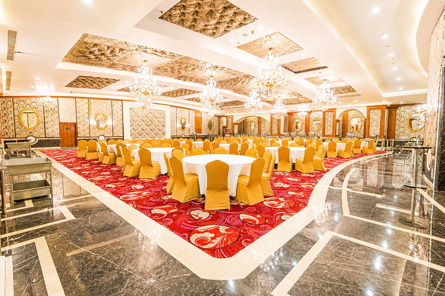Un salón de banquetes con mesas redondas, sillas amarillas y una alfombra roja.