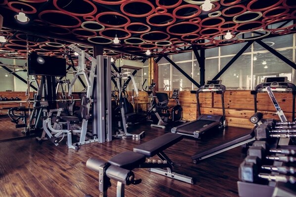 Ein Fitnessraum mit unterschiedlichen Trainingsgeräten, Laufband und einer Bank.