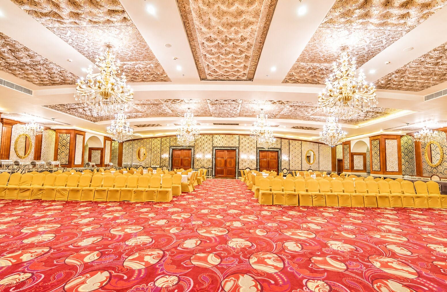 Un amplio salón de conferencias con hileras de sillas amarillas, decoraciones ornamentales en el techo y candelabros.
