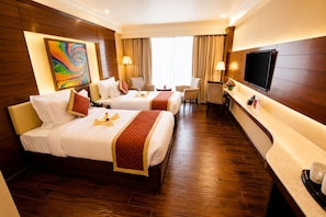 A hotel room with two beds, a desk, a TV, and a painting on the wall. - Shakun Hotels & Resorts Jaipur (Jaipur)