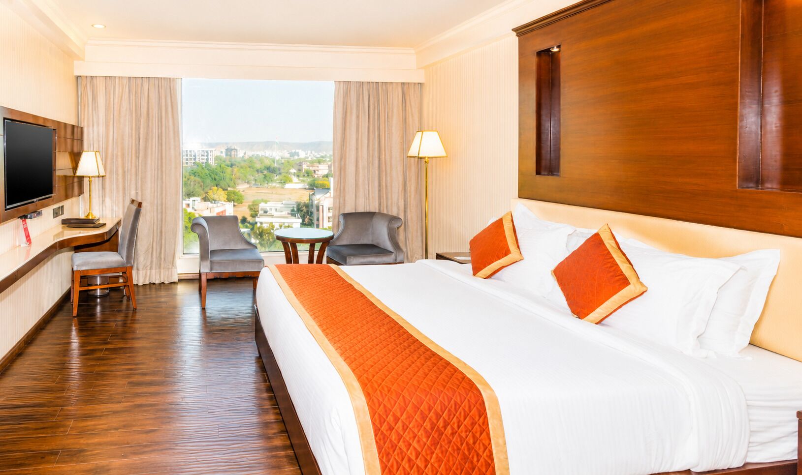 Habitación de hotel con una cama grande, un escritorio, un televisor y vistas a la ciudad.