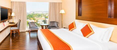 Habitación de hotel con una cama grande, un escritorio, un televisor y vistas a la ciudad.