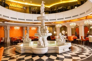 Un vaste hall d’hôtel avec une fontaine centrale, de nombreux espaces de restauration et des lustres somptueux.