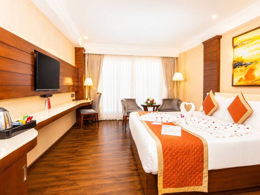 Habitación de hotel con cama, escritorio, silla, televisión y un cuadro en la pared.