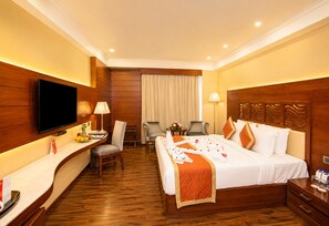 Ein Hotelzimmer mit Bett, Schreibtisch, Stuhl, Fernseher und einem Fenster mit Vorhängen.