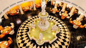 Eine Hotelhalle mit einer zentralen Springbrunnen, mehreren Essplätzen und einem Schachbrettmuster auf dem Boden.