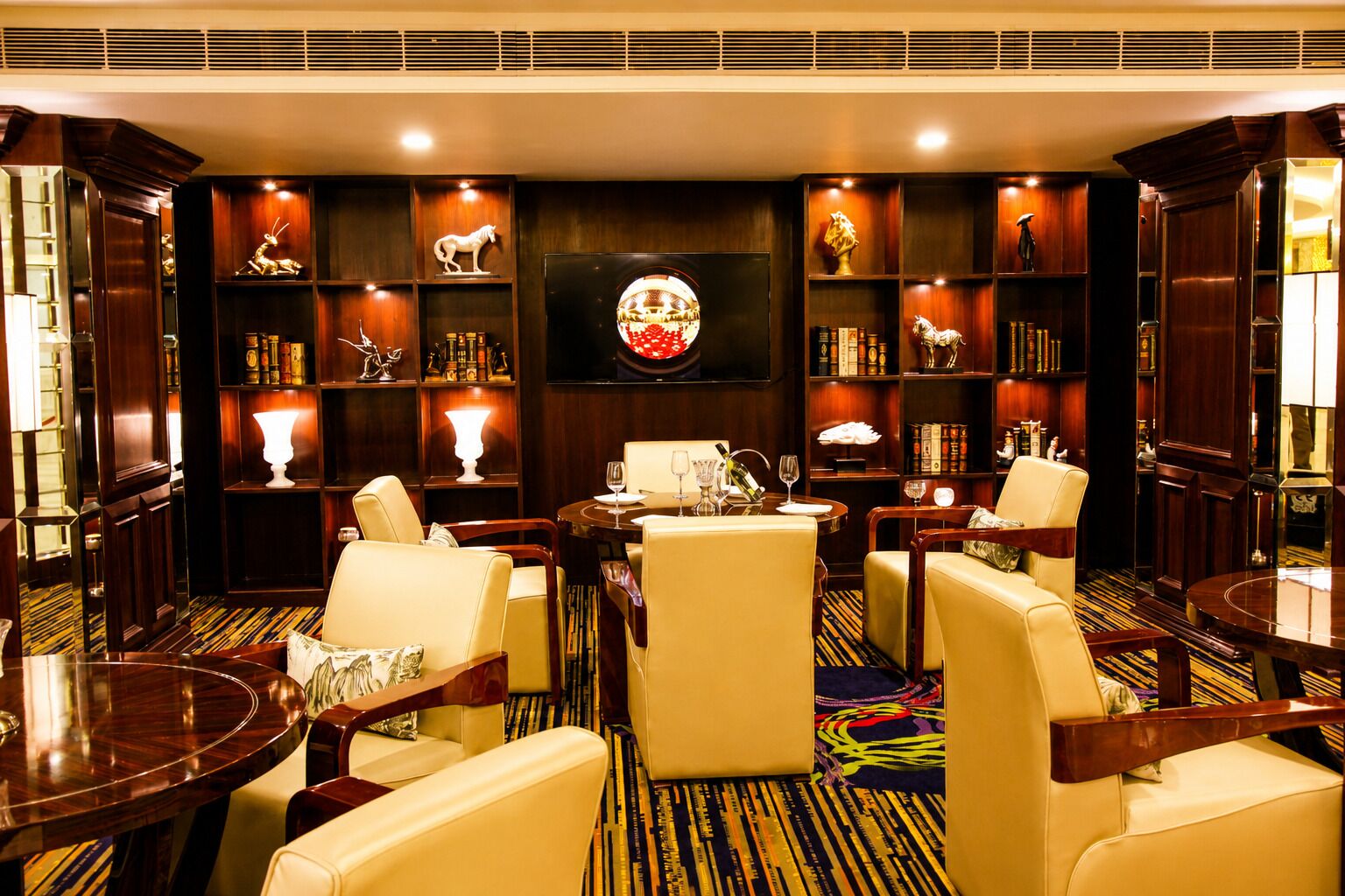 Een hotel lobby met lederen fauteuils, een ronde tafel en een boekenplank met decoratieve objecten.