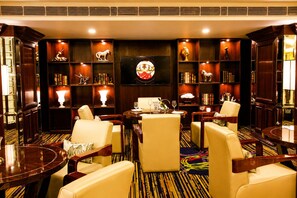 A hotel lounge with leather chairs, a round table, and a bookshelf with decorative items. - Shakun Hotels & Resorts Jaipur (Jaipur)