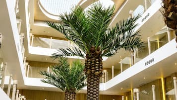 Un atrio de varios niveles con palmeras, zonas de estar y un diseño arquitectónico moderno.