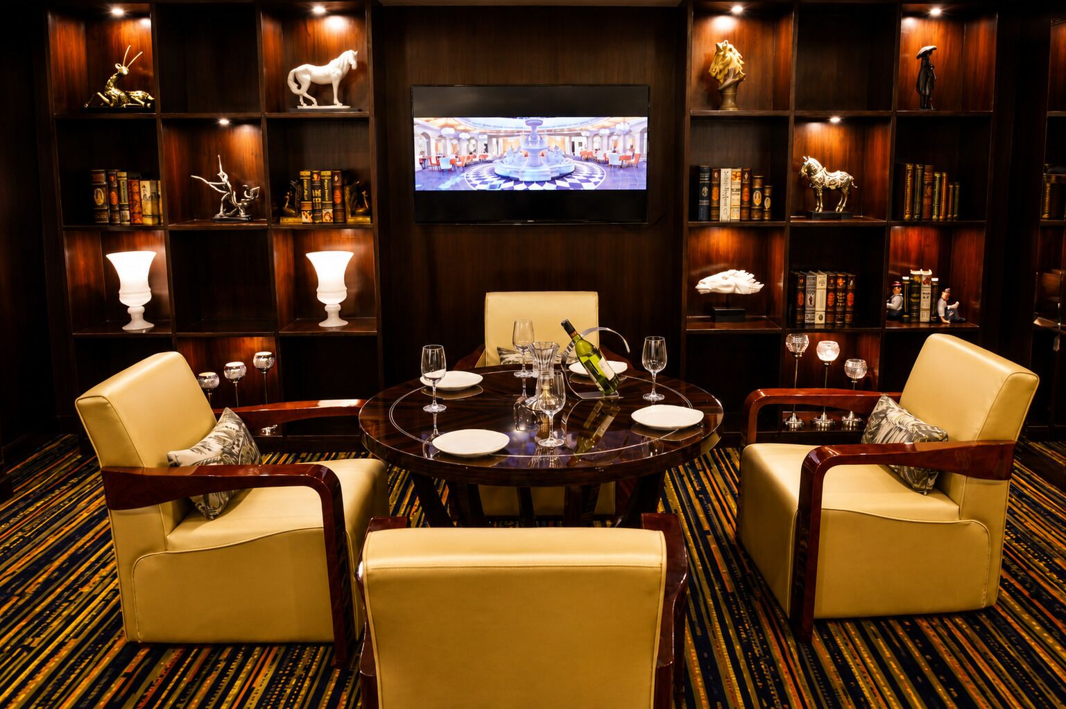 A hotel room with a round dining table, two chairs, a television, and bookshelves.