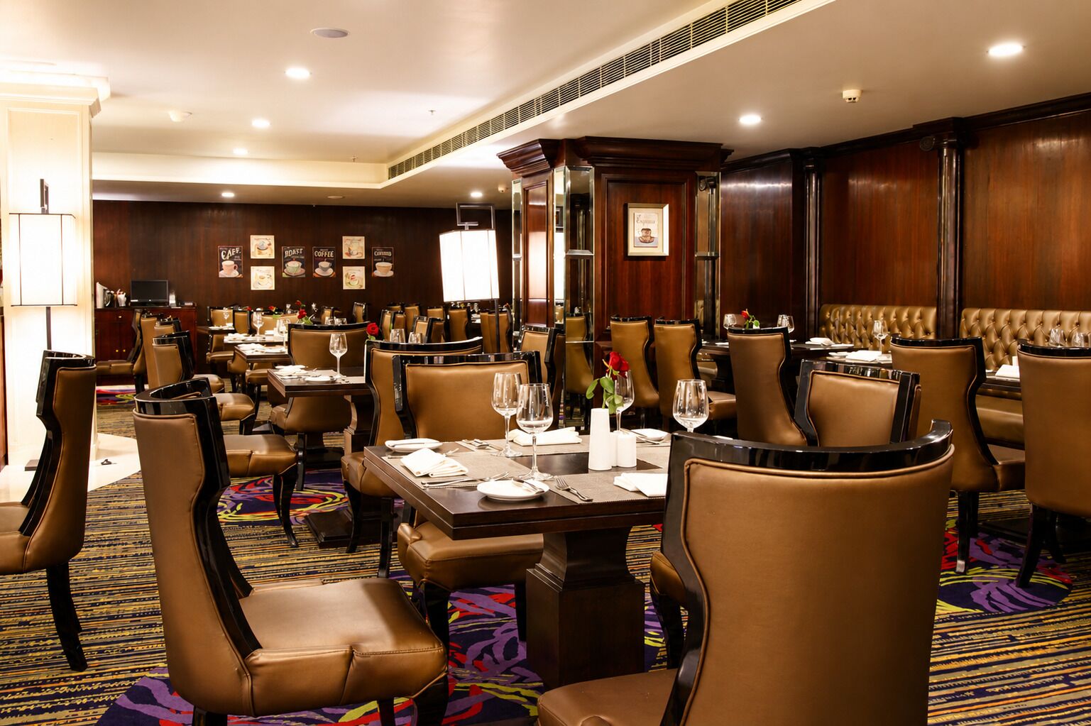 A hotel dining area with multiple tables and chairs, each set with plates, glasses, and cutlery.