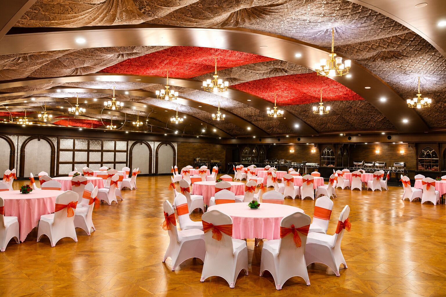 A banquet hall with round tables, white chairs with orange sashes, and a high ceiling with intricate patterns.