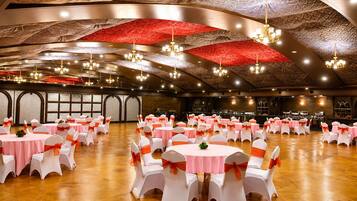 A banquet hall with round tables, white chairs with orange sashes, and a high ceiling with intricate patterns.