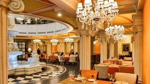 A luxurious dining area with ornate chandeliers, marble columns, and a central fountain.