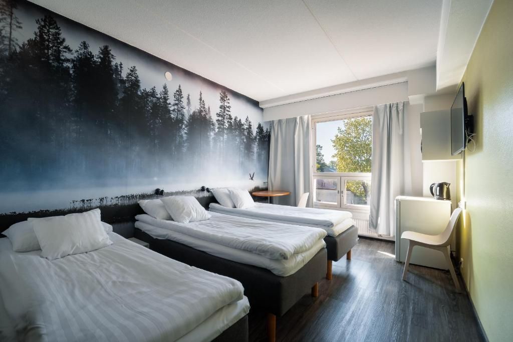 A hotel room with two beds, a desk, a chair, a television, and a large forest mural on the wall.