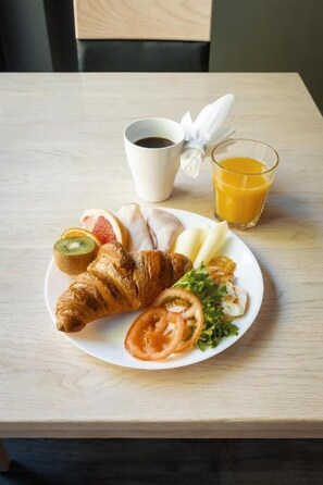 A breakfast setting with a croissant, sliced fruit, a glass of orange juice, and a cup of coffee on a wooden table. - Hotelli Uninen Loviisa (Loviisa)