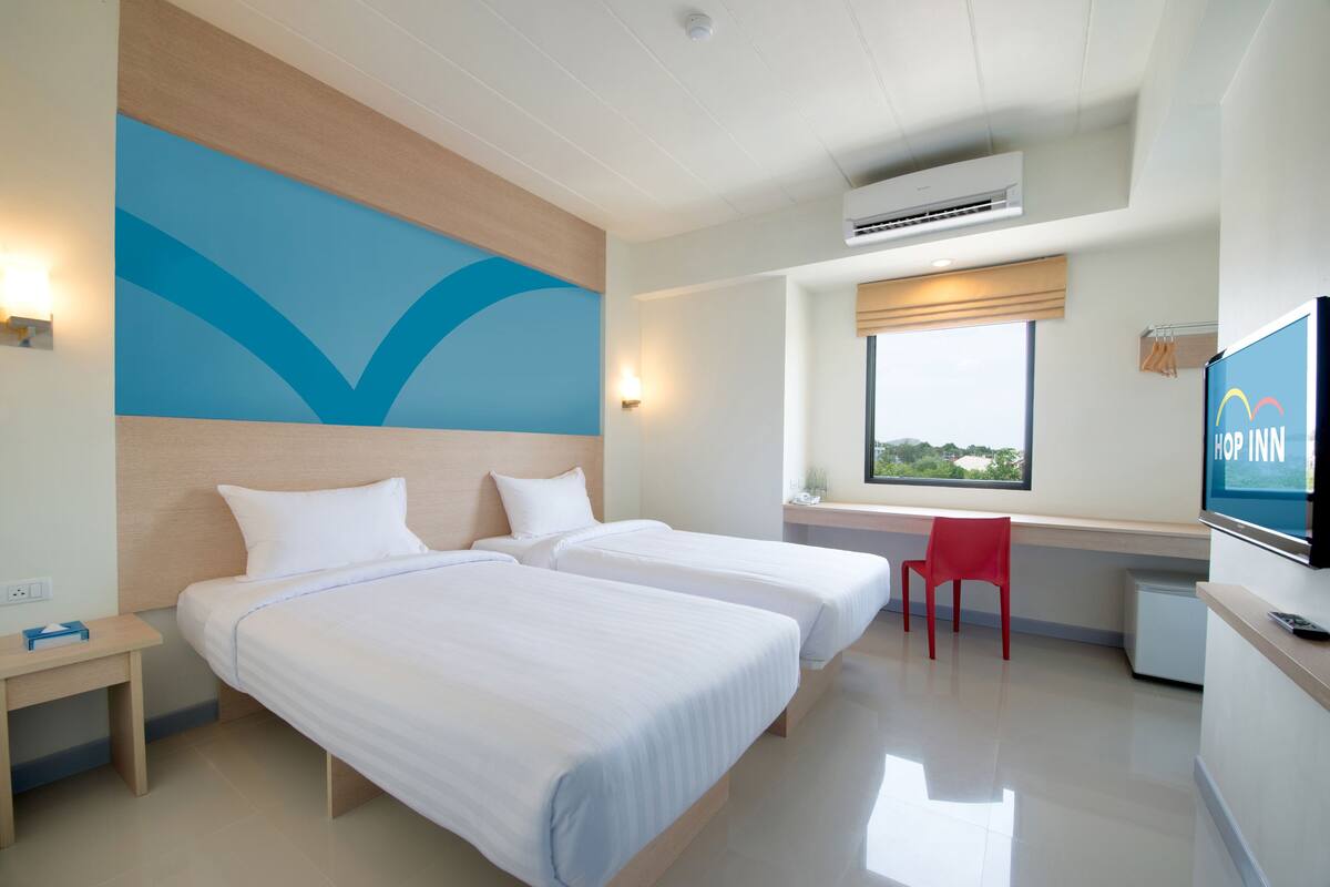 A hotel room with two beds, a desk, a TV, and a window with a view.