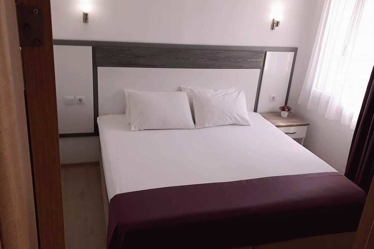 A neatly made bed with white linens and a dark headboard.
