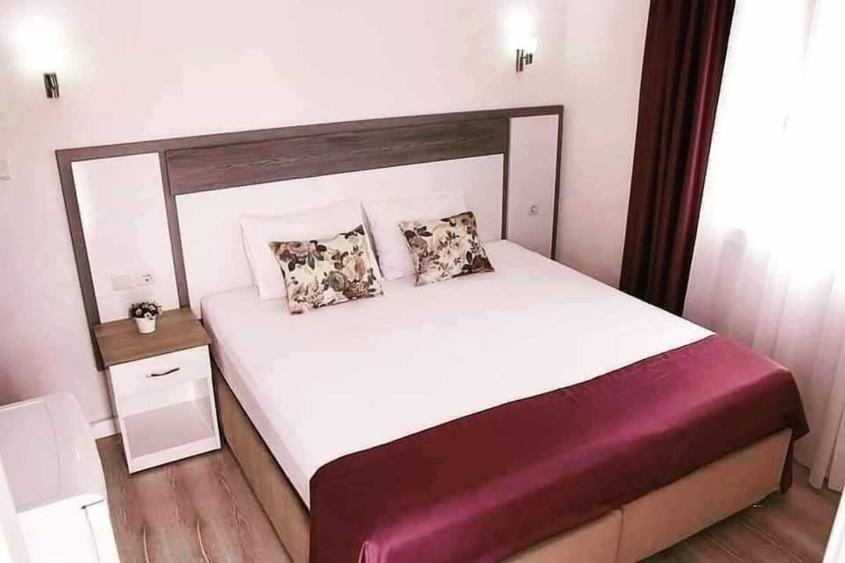 A neatly made bed with a wooden headboard, two pillows, and a red throw blanket.