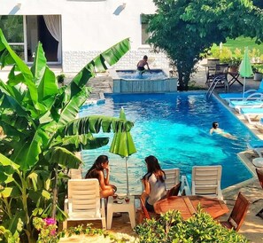 Zona de piscina con sillones, una mesa y una persona nadando.