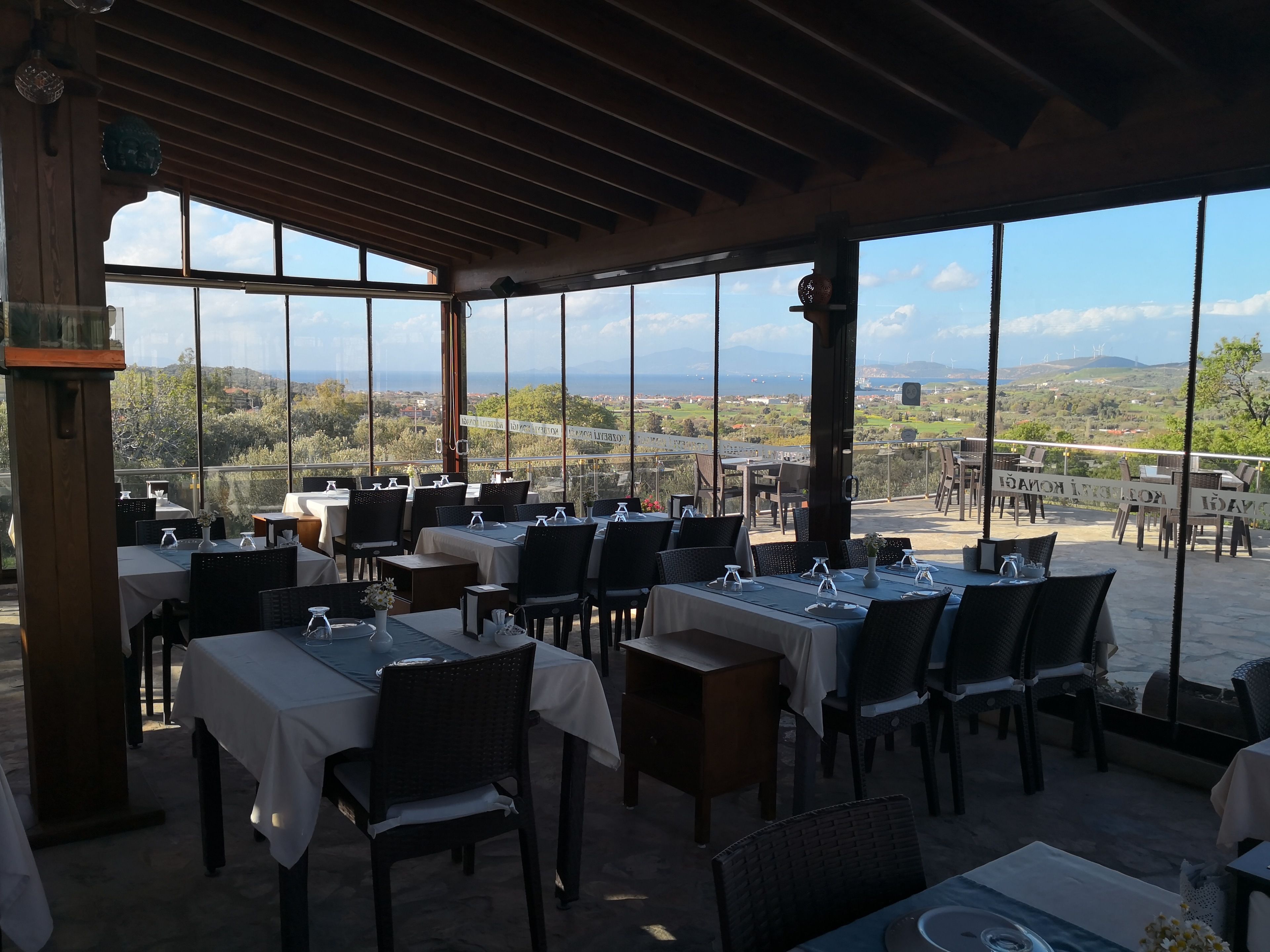 Un restaurante con mesas y sillas dispuestas bajo un porche cubierto, con amplias ventanas que ofrecen vistas al campo.