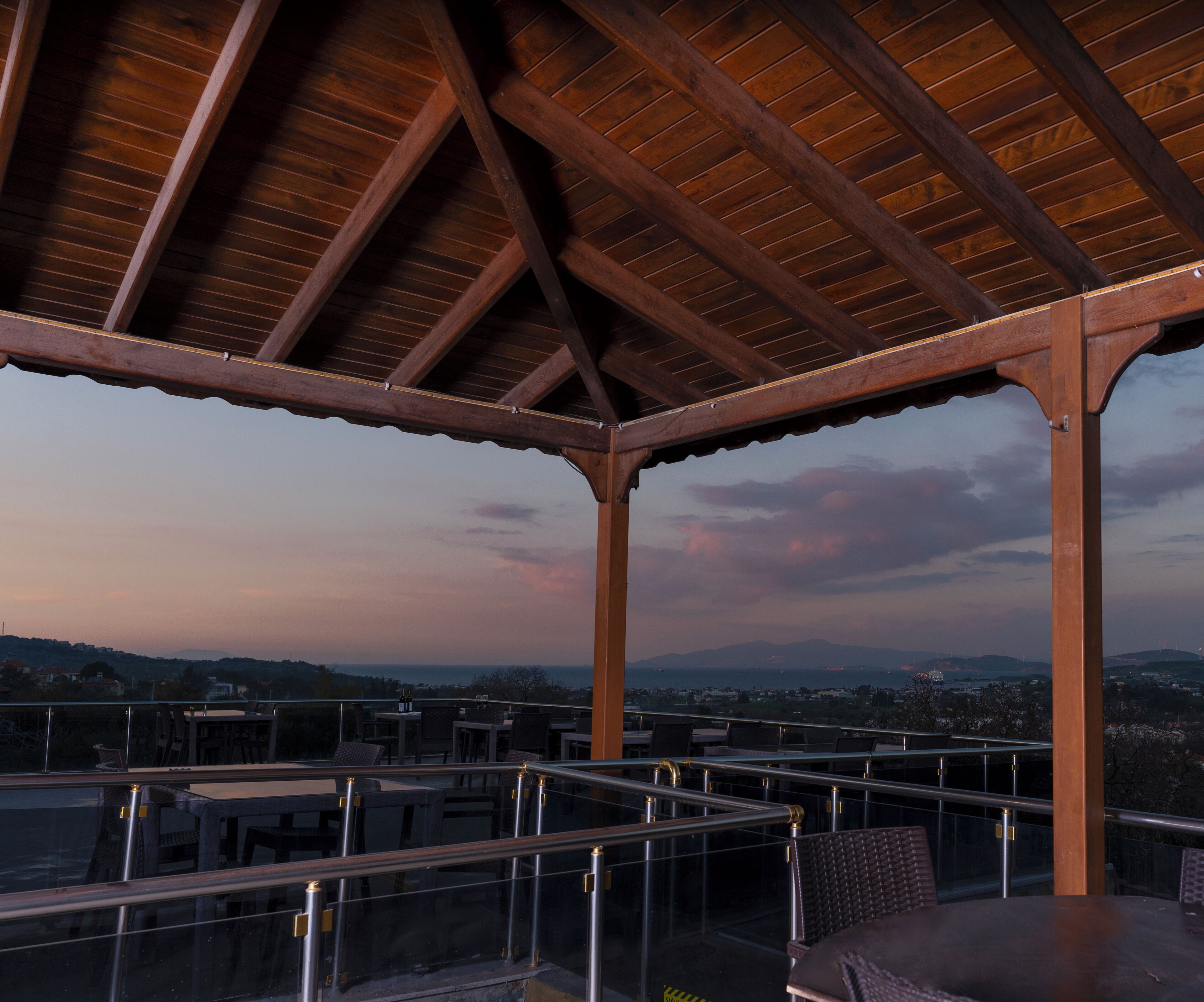 Un espace extérieur abrité, doté de tables et de chaises, offrant une vue sur le paysage urbain et les montagnes.