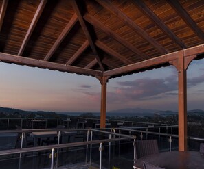 A covered outdoor seating area with tables and chairs, overlooking a cityscape and mountains.