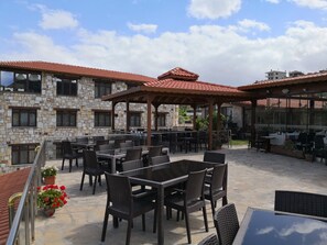 An outdoor patio area with stone walls, multiple tables and chairs, and a pergola structure.