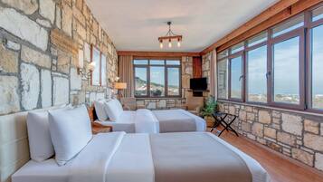 Une chambre d’hôtel avec des murs en pierre, deux lits, une télévision et de grandes fenêtres donnant sur un paysage.