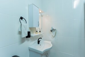 A modern bathroom with white tiles, a white sink, a black faucet, a towel rack, a mirror, and a wall-mounted telephone.
