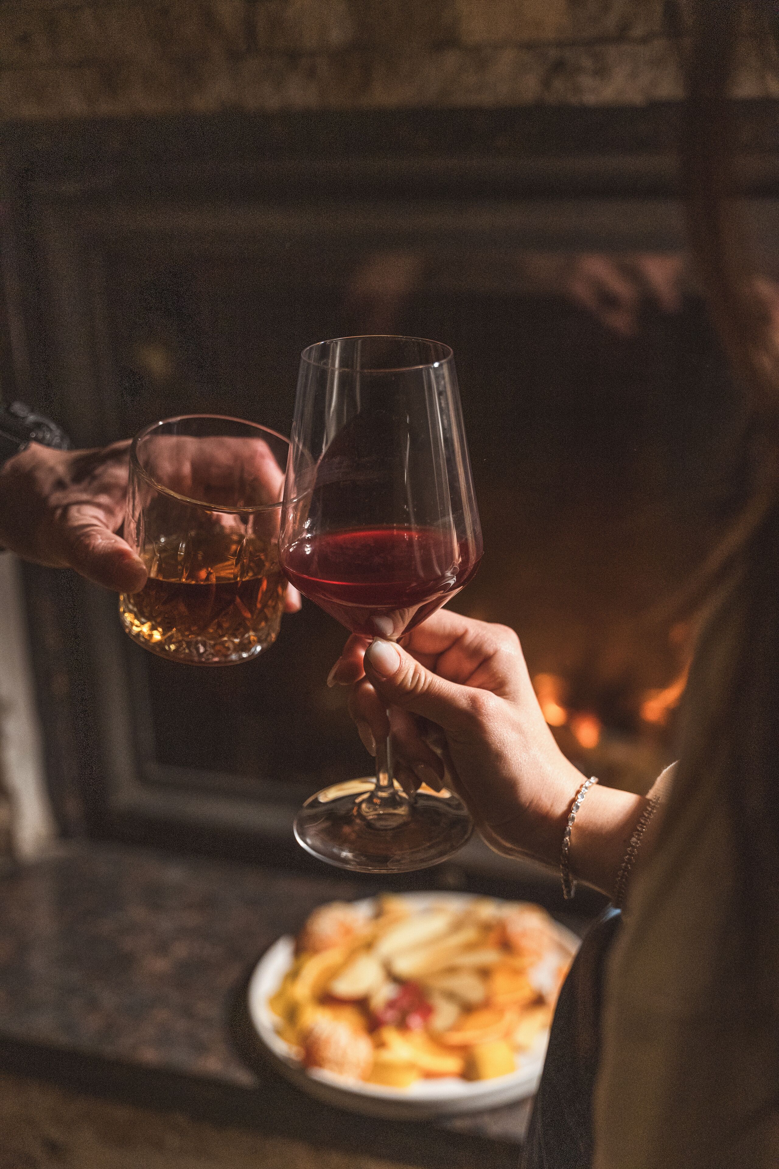 Deux personnes, chacune tenant un verre de vin, l’une contenant un liquide clair et l’autre du vin rouge, se tiennent devant une cheminée.