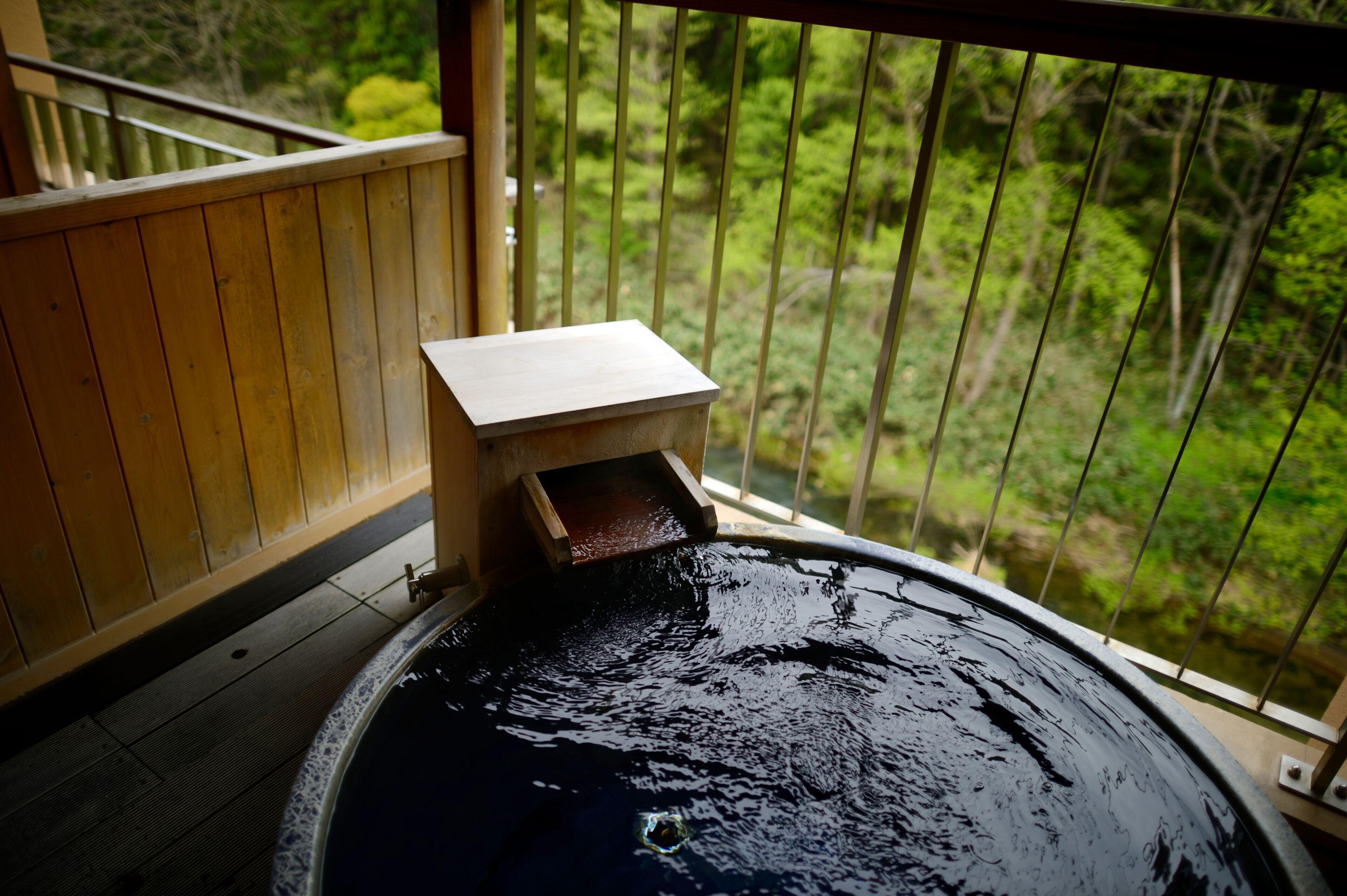 A hot spring bath with a wooden deck and a view of a forested area.