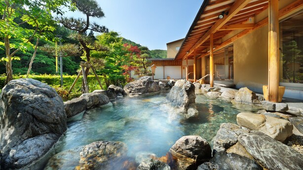 A traditional Japanese onsen with a wooden structure and a clear hot spring surrounded by rocks.