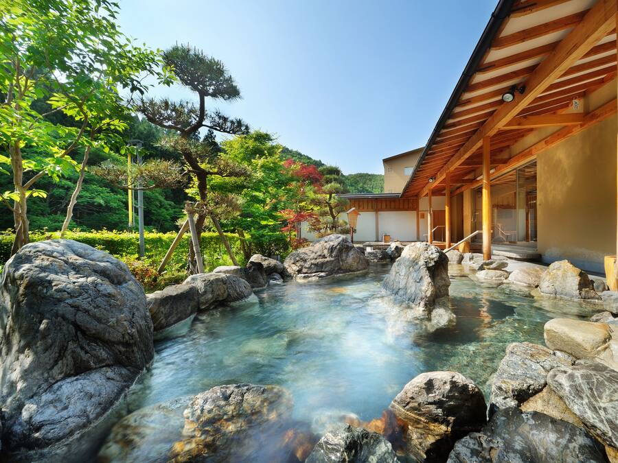 A traditional Japanese onsen with a wooden structure and a clear hot spring surrounded by rocks.
